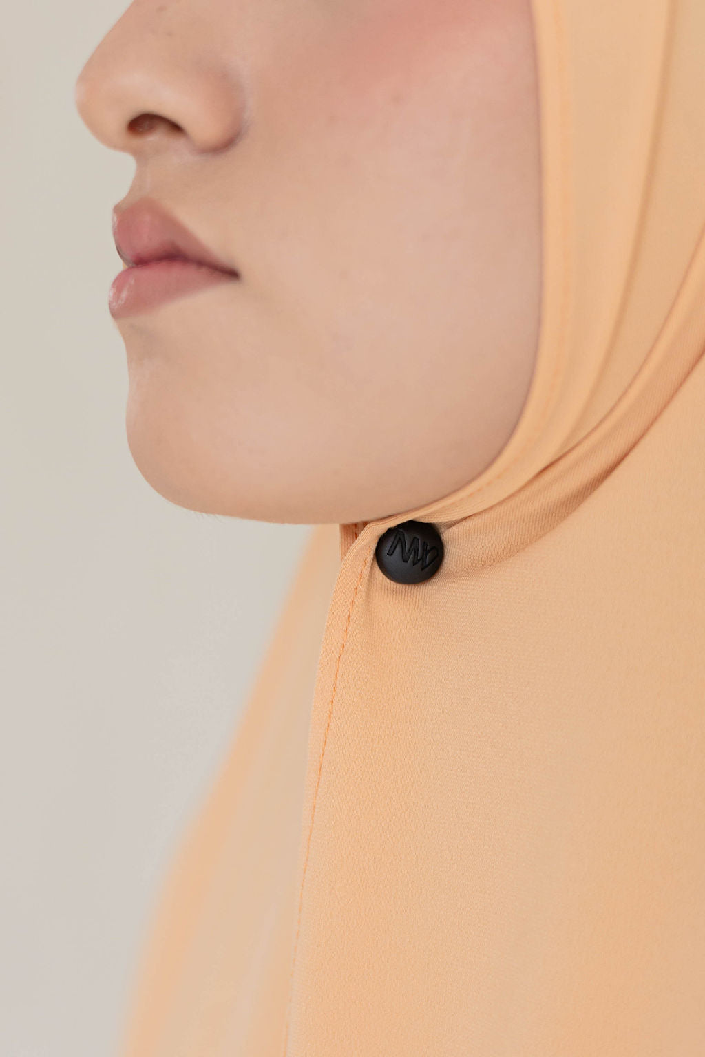 Close-up model wearing Naleya wear logo black hijab magnets with strong hold on pastel orange premium jersey scarf