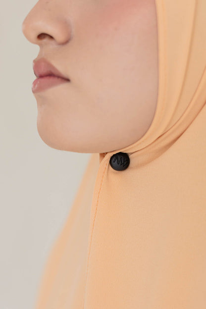 Close-up model wearing Naleya wear logo black hijab magnets with strong hold on pastel orange premium jersey scarf
